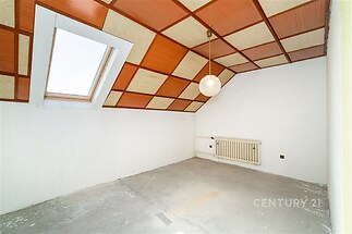 Podkrovní pokoj s dřevěným obkladem na stropě, velké střešní okno a bílými stěnami nabízí světlý prostor k úpravám.