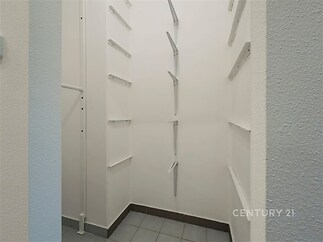 Úložný prostor se světlými stěnami a dlažbou na podlaze, vybavený regálovými policemi. Ideální pro uskladnění v moderním bytě.