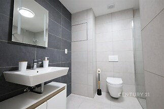 Moderní koupelna s elegantní dlažbou, závěsné WC a stylové umyvadlo. Neutrální barvy a minimalistický design vytvářejí čistý vzhled.