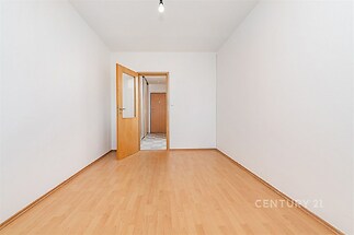 Prázdná místnost s parketovou podlahou, světlé stěny a dřevěné dveře, připravená k úpravám a zařizování.