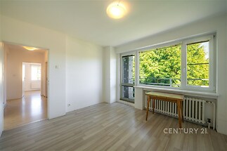 Světlý obývací pokoj s velkými okny, moderní parketovou podlahou a výhledem do zeleně, ideální pro světlé a vzdušné bydlení