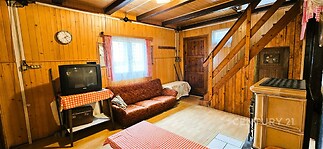 Obývací pokoj s dřevěným obložením, starožitným nábytkem a dřevěnými schody. V místnosti jsou parkety a starožitná kamna pro rustikální vzhled.