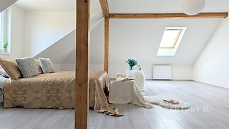 Světlá ložnice s dřevěnými trámy, laminátovou podlahou a střešním oknem, poskytuje moderní a útulnou atmosféru.