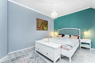 Světlá ložnice s parketovou podlahou, moderní světlo, dvojlůžko a barevná výmalba stěn.