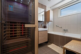 Moderní koupelna s dlažbou, infrasaunou a velkým oknem zajišťujícím přirozené světlo, kvalitní dřevěný nábytek a elegantní vanou.