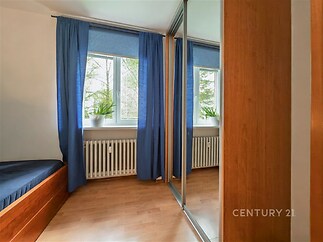 Ložnice s parketovou podlahou a vestavěnými skříněmi, světlý prostor díky velkým oknům a modrým závěsům.