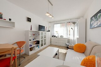 Světlý obývací pokoj s moderním nábytkem, parketová podlaha a velká okna zajišťující dostatek přirozeného světla.