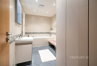 Moderní koupelna s dlažbou, prostornou vanou a velkým umyvadlem, útulná atmosféra díky bodovému osvětlení a decentní mozaikové obklady