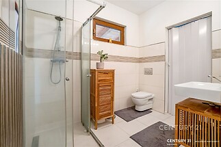 Moderní koupelna s dlažbou, sprchovým koutem a dřevěnou skříňkou, světlá a elegantní, ideální pro komfortní bydlení.