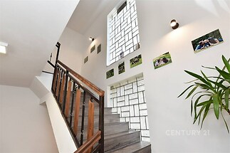 Světlo schodiště s moderní dlažbou a dřevěným zábradlím, velké okno poskytující přirozené světlo, dekorativní fotografie na stěnách.