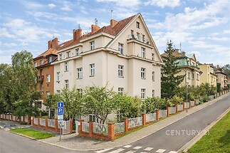 Vícepatrový činžovní dům s klasickou fasádou, šikmou střechou a zahradou; klidná ulice, rezidenční čtvrť vhodná pro rodiny.