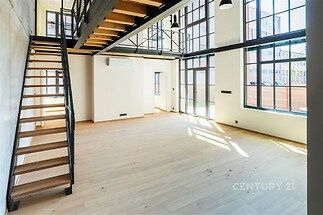 Světlý obývací pokoj s parketovou podlahou, velká okna a moderní průmyslový styl.