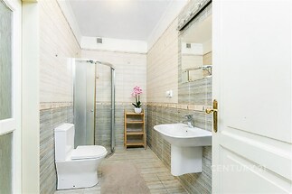 Moderní koupelna s dlažbou, sprchovým koutem a velkým zrcadlem. Světlý interiér, decentní obklady a bílá sanita vytvářejí elegantní vzhled.