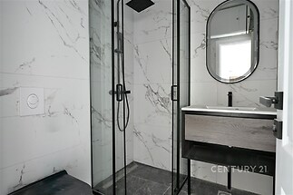 Moderní koupelna s mramorovými obklady, proskleným sprchovým koutem a elegantním zrcadlem, stylová a nadčasová úprava.