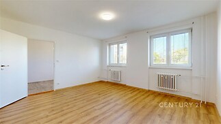 Světlý obývací pokoj s parketovou podlahou, velká okna a moderní úprava, ideální pro rodinné bydlení nebo investici.