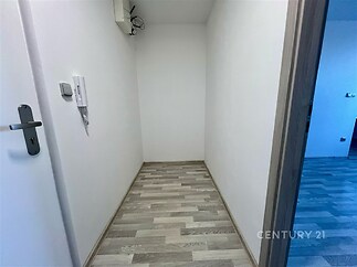 Úzká chodba s parketovou podlahou, čistě bílé zdi a moderní interkom.