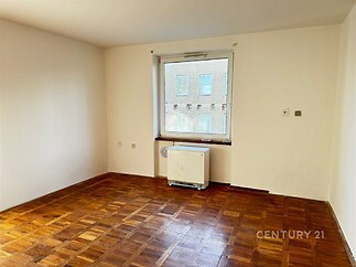 Světlý obývací pokoj, parketová podlaha, velké okno, čisté bílé stěny, světlý interiér.