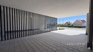 Venkovní terasa s moderní dlažbou, vybavená stylovými sloupy, poskytuje prostorný a funkční exteriér pro relaxaci nebo parkování.