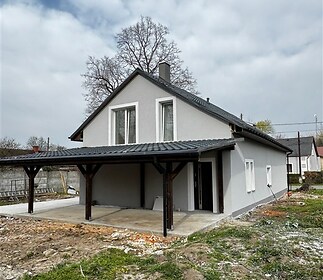 Zrekonstruovaný rodinný dům s moderní fasádou, velkými okny a prostorným krytým parkovacím stáním na zahradě.