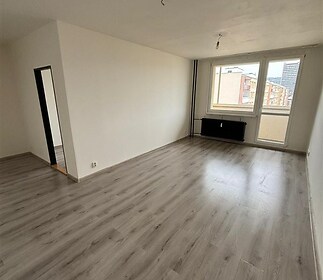 Světlý obývací pokoj s laminátovou podlahou, velká okna, světlý interiér, výhled na město, moderní styl, renovovaný prostor.