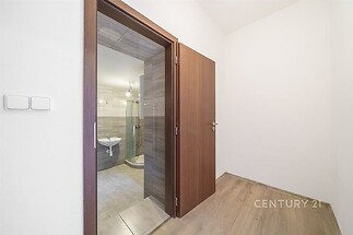 Vstupní hala s dřevěnou podlahou a dveřmi vede do moderní koupelny obložené dlaždicemi, čisté linie a světlé povrchy dominují interiéru.