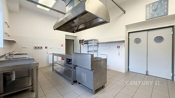 Průmyslová kuchyň s nerezovými povrchy, dlažbou a moderními spotřebiči. Vhodná pro gastronomické provozy.