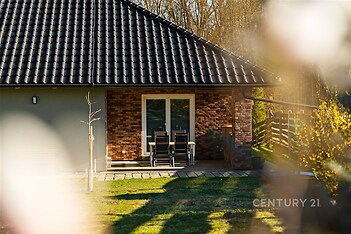 Exteriér domu s terasou, cihlovým obkladem a velkými okny, moderní styl. Udržovaná zahrada dodává příjemnou atmosféru.