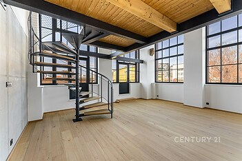 Světlý obývací pokoj s dřevěnou podlahou a velkými okny, moderní točité schodiště, industriální styl, vysoké stropy.