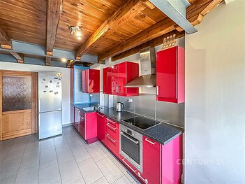 Moderní kuchyň s červenými skříněmi, nerezovými spotřebiči a dlažbou. Dřevěný strop dodává místnosti stylový vzhled.