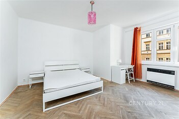 Prostorná ložnice s parketovou podlahou, velká okna a moderní nábytek. Světlé provedení s výhledem do ulice.