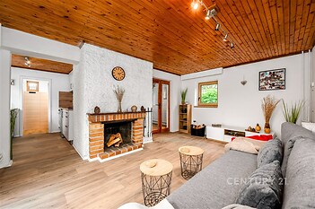 Útulný obývací pokoj s krbovými kamny, dřevěným stropem a parketovou podlahou. Světlý interiér nabízí moderní styl a pohodlí.