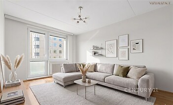 Světlý obývací pokoj s parketovou podlahou, moderní sedačkou a velkými okny, které zajišťují přirozené světlo.