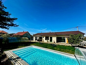 Zahrada s bazénem u moderního domu, terasa s velkými okny, udržovaná zeleň, ideální pro rodiny hledající klidný a komfortní životní styl.