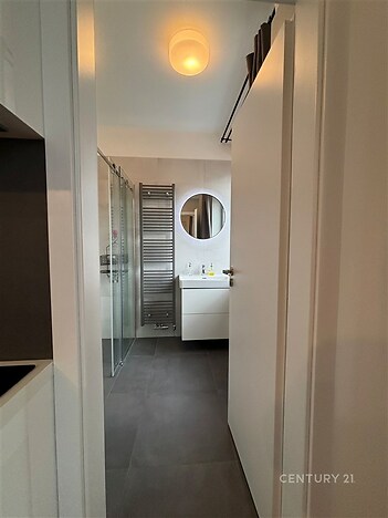 Moderní koupelna s dlažbou, sprchovým koutem a kulatým zrcadlem, vybavená žebříkovým radiátorem, tvoří elegantní a funkční prostor.