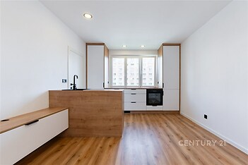 Moderní kuchyň s parketovou podlahou, velká okna poskytující dostatek světla, vestavěné skříně a minimalistický design