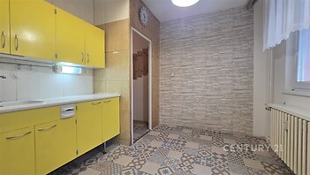 Kuchyň v retro stylu s výraznými žlutými skříňkami, dlažbou s vintage vzorem a světlými kamennými obklady na zdech