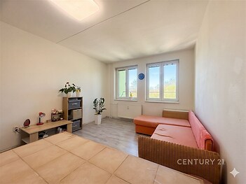 Světlý obývací pokoj s velkými okny, moderní podlahou a rekultivovaným interiérem, nabízí komfort a styl pro bydlení.