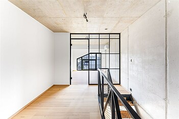 Průmyslová chodba s parketovou podlahou, industriálním zábradlím a velkými okny, moderní design s betonovými stropy.