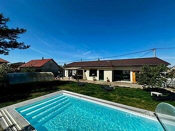 Prostorná zahrada s moderním bazénem, travnatým povrchem a terasou, ideální pro relaxaci v klidné lokalitě.