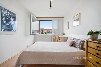 Světlá ložnice s parketovou podlahou, velkými okny a moderním nábytkem, poskytuje útulné a příjemné prostředí.