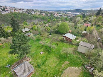 Přírodní pozemek s výhledem na krajinu, obklopen stromy a keři, v klidné lokalitě s rekreačními chatami a zelení, ideální pro milovníky přírody.