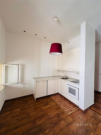 Světlá kuchyň s dřevěnou podlahou, moderními bílými skříňkami a stylovým červeným osvětlením, ideální pro útulné bydlení