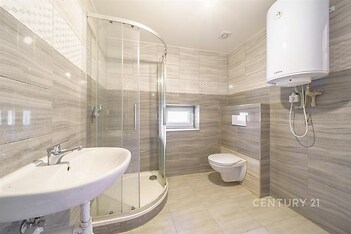 Prostorná koupelna s moderními obklady, sprchovým koutem a závěsnou toaletou, světlá dlažba, bojler na stěně.