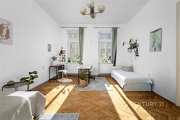 Světlý obývací pokoj s parketovou podlahou, velká okna s bílými rámy, moderní dekorace a minimalistický nábytek, ideální pro rekreační obývání.