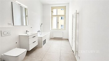 Světlá koupelna s moderní keramickou dlažbou, velkým oknem a nástěnným topením, čistý a minimalistický design.