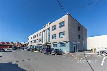 Moderní komerční budova s velkými okny a parkovacími místy. Stavba ve světlých barvách nabízí flexibilní kancelářské prostory.