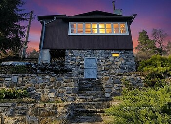 Chata s kamennou fasádou, velkými okny a zahradou, podvečerní atmosféra, klidná lokalita v přírodě.