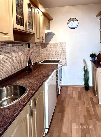 Úzká kuchyň s dřevěnými skříňkami, moderními spotřebiči a parketovou podlahou, nabízí útulný prostor pro vaření.