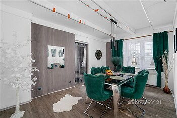 Jídelna s moderním designem, luxusní zelené čalounění, tmavá dřevěná podlaha, velká okna se závěsy, elegantní osvětlení, světlý interiér.