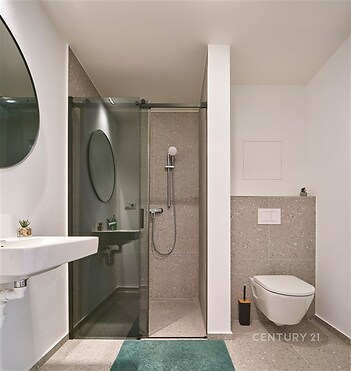 Moderní koupelna s dlažbou, prosklený sprchový kout a minimalistický design, elegantní umyvadlo a závěsné WC pro svěží vzhled.